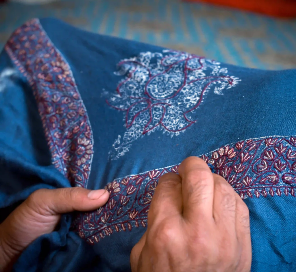 artisan doing sozini work on a blue kashmiri pashmina shawl
