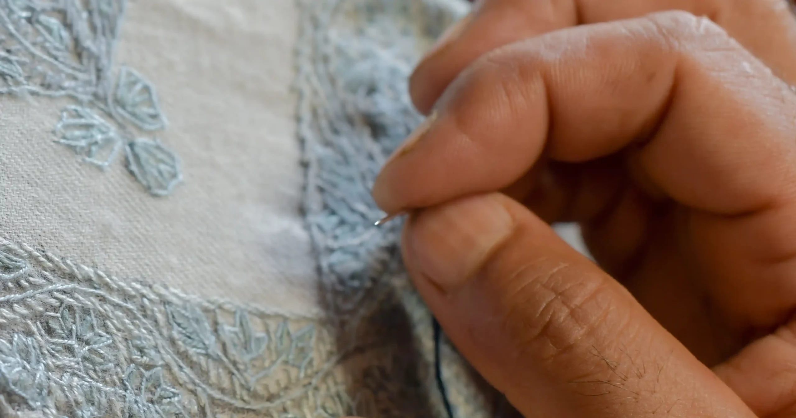 artisan doing sozni embroidery on a white shawl in kashmir